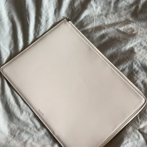 Beige datorväska från Holdit - Stilren och tunn datorväska från Holdit i beige syntetmaterial. Väskan har dragkedja runtom och är fodrad på insidan för extra skydd. Perfekt för att bära med sig laptopen på ett snyggt och minimalistiskt sätt. Storlek 35,25 cm, inte i originalförpackning, aldrig andvänt 