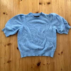 Ljusblå stickad tröja från Vero Moda - Superfin ljusblå stickad tröja från Vero Moda i storlek XS. Tröjan har korta puffärmar och ribbade muddar vid ärmslut och nederkant. Perfekt för dig som gillar en söt och enkel stil med en twist!