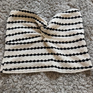 Randig bandeau tubtopp från Amisu - Superfin bandeau tubtopp från Amisu i svart och vitt med stickat randigt mönster. Toppen har en twistad detalj framtill och är axelbandslös, perfekt för varma dagar. Materialet är mjukt och stretchigt, vilket gör den bekväm att bära. Den har ingen storlek men skulle säga runt xs/s