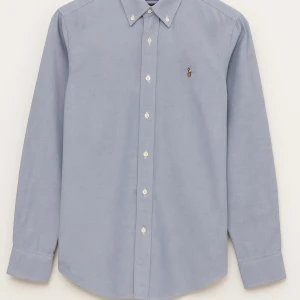 Polo Ralph Lauren slim fit skjorta - Klassisk ljusblå skjorta från Polo Ralph Lauren i slim fit-modell. Skjortan har button down-krage, långa ärmar och broderad logga på bröstet. Tillverkad i mjuk bomull och stängs med vita knappar framtill. Perfekt för en clean och stilren look.