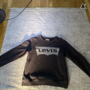 Svart sweatshirt från Levi's med logga - Cool svart sweatshirt från Levi's med stor vit logga framtill. Tröjan har rund halsringning, långa ärmar och ribbade muddar. Perfekt för en avslappnad stil och funkar året runt. Materialet är mjukt och skönt, troligtvis bomull eller bomullsblandning.