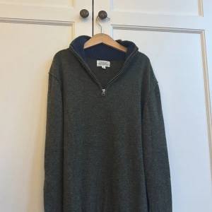 Mörkgrå stickad half zip från Hartford - Mysig mörkgrå stickad tröja från Hartford med hög krage och half zip-dragkedja. Insidan av kragen är blå och ger en snygg kontrast. Perfekt för lager-på-lager och chill höst- och vinterdagar. Ordinarie pris 4000