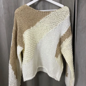 Beige och vit stickad tröja - Säljer en chunky stickad tröja i beige och vitt med coola blockmönster. Tröjan har en avslappnad passform och långa ärmar, perfekt för att mysa i under kyliga dagar. Superfin till jeans eller kjol för en chill look.
