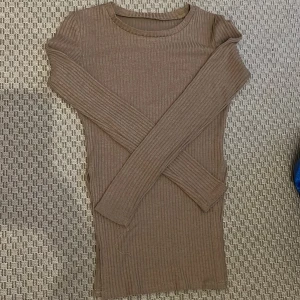 Ribbad brun långärmad tröja - Säljer en ribbad, kroppsnära tröja i brun nyans. Tröja har lång ärm, slits på vardera sida, rund halsringning och är tillverkad i ett stretchigt material som sitter snyggt på kroppen. Perfekt för dig som gillar en enkel men stilren look.