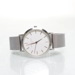 Silverfärgad klocka från Rosefield - Stilren klocka från Rosefield med rund vit urtavla och minimalistiska silverfärgade index. Armbandet är i meshad metall och har ett smidigt spänne. Perfekt accessoar för dig som gillar en clean och modern look.        Behöver ett nytt batteri.