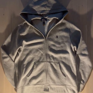 Grå Ralph Lauren hoodie - Säljer denna sköna Ralph Lauren hoodie. Väldigt bra skick och tvär skön. Säljer den för att den tyvärr är för stor för mig. Storleken är 170/88 eller XL i barn storlek. OBS köp ej här, köp på min Vinted istället (juliuslen.sell)