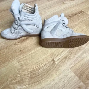 Beige Isabel Marant sneakers i mocka - Snygga beige sneakers från Isabel Marant i mjuk mocka med högt skaft och breda kardborreband.  Dem är väl använda och säljs därav för 1279kr! Orginal pris 4999kr. Dem är äkta och även lådan kommer på köpet! De är köpta på Jackie! 