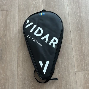 Paddel rack & Väska  - Jag säljer ett paddel rack ifrån tretorn mycket bra skick och ordinarie pris ligger på 3500kr. Säljer även  en svart padelväska från Vidar of Båstad med vit logga och svensk flagga på framsidan. Väskan har en droppformad design, dragkedja runtom och ett praktiskt handtag. Perfekt för att bära och skydda ditt padelracket till och från banan.