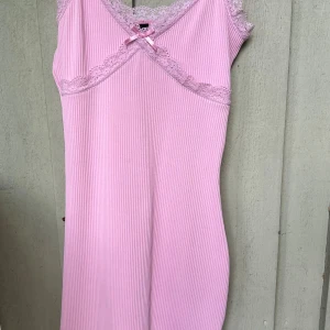 Rosa ribbad spetsklänning H&M XS - Supersöt ljusrosa kortklänning från H&M Divided i ribbad bomull med spetsdetaljer vid halsringningen och axlarna. Klänningen har en liten rosett framtill och är ärmlös, perfekt för sommarens varma dagar. Sitter snyggt med slim passform.