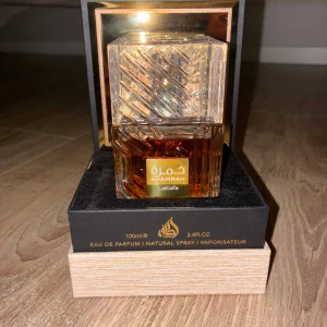 Lattafa Khamrah Eau de Parfum 100ml - Lattafa Khamrah är en lyxig parfym i en tung, fyrkantig glasflaska med vackert mönstrad yta och guldiga detaljer. Doften kommer i en exklusiv svart och träfärgad ask med gulddetaljer. Flaskan rymmer 100 ml och har en varm bärnstensfärgad vätska.