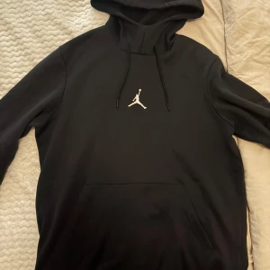Svart Jordan hoodie med logga - Svart hoodie från Jordan med den klassiska Jumpman-loggan i vitt på bröstet. Tröjan har huva med snörning och en stor magficka framtill. 