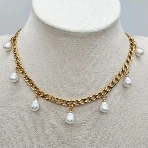 Guldfärgat halsband med pärldroppar - Stilrent halsband med chunky guldfärgad kedja och sju droppformade vita pärlor som hänger längs hela halsbandet. Perfekt statement-piece för att lyfta din look med en touch av lyx och trendig vibe.