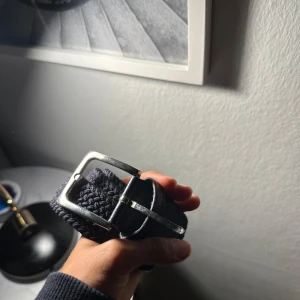 Mörkblått flätat bälte från Hugo - Snyggt mörkblått bälte från Hugo med flätad design och detaljer i skinn. Bältet har ett klassiskt silverfärgat spänne och stilren look som passar till jeans eller chinos. Perfekt accessoar för att lyfta din outfit.