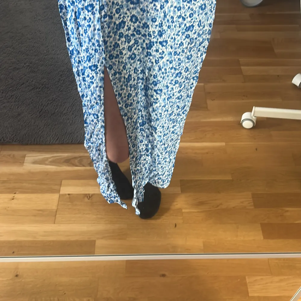 Säljer en vacker blommig långklänning från FBSister i blått och vitt. Klänningen har en öppen rygg och en slits framtill. Den är ärmlös med knytning vid bysten, perfekt för sommarens varma dagar.. Mekot.