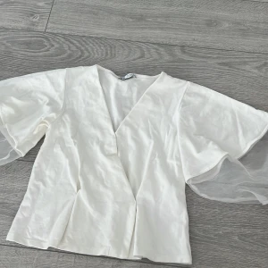 Vit blus från Zara - Säljer en elegant vit blus från Zara med v-ringning och korta, luftiga ärmar i transparent tyg. Perfekt för en stilren look. Passar till både jeans och kjol. 🌟