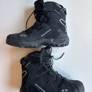 Svarta vinterkängor från Salomon - Säljer ett par robusta svarta vinterkängor från Salomon. De har en hög design med snörning och är perfekta för kalla dagar. Kängorna har en slitstark sula och är gjorda för att klara tuffa förhållanden.