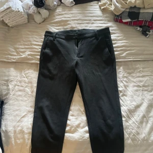 Svarta kostymbyxor från Gabba - Snygga svarta kostymbyxor från Gabba med dragkedja och knapp framtill. Perfekta för en stilren look. Byxorna har en klassisk passform och är tillverkade i ett bekvämt material.