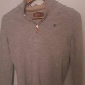 Grå tröja med dragkedja från Morris - Säljer en stilren grå tröja från Morris med dragkedja vid halsen. Tröjan har en liten broderad logga på bröstet och är perfekt för både vardag och mer avslappnade tillfällen. Den är i storlek S men sitter som XS