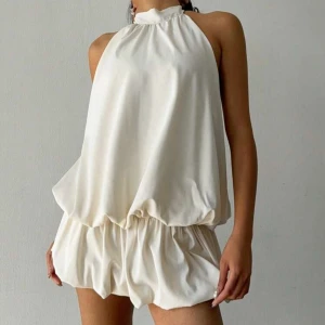 Vit axelbandslös klänning - Snygg vit axelbandslös klänning med halterneck och knytning i nacken. Den har en luftig passform med volangdetaljer och en elastisk midja. Helt ny