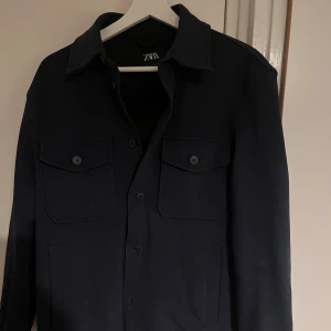 Mörkblå jacka från Zara - Snygg mörkblå jacka från Zara med knappar framtill och två bröstfickor med lock. Perfekt för en stilren look. Jackan har en klassisk krage och är tillverkad i ett robust material. De är storlek S men passar även till de som har M! 