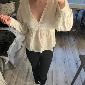 Vit blus med spetsdetaljer - Säljer en vacker vit blus med spetsdetaljer och v-ringning. Blusen har långa ärmar och en luftig passform, perfekt för en stilren look. Passar bra till både jeans och kjol.