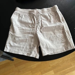 Beige shorts från Jack & Jones - Säljer ett par stilrena beige line shorts från Jack & Jones. De har en elastisk midja med snörning och är perfekta för varma dagar. Shortsen har en bakficka och är tillverkade i ett lätt och bekvämt material.