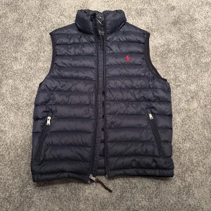 Mörkblå dunväst från Polo Ralph Lauren - Säljer en snygg mörkblå dunväst från Polo Ralph Lauren. Västen är i nyskick då den inte använts så mycket. Nypris ligger på 3500.  Priset inte hugget i sten för snabb affär 