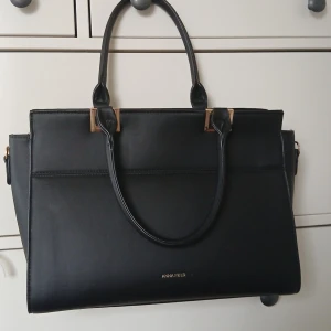 Svart handväska från Anna Field - Elegant svart handväska från Anna Field med guldfärgade detaljer och dragkedja. Allt är fullt fungerande. Det ända är att axelremen inte följer med då jag inte fick den när jag beställde väskan, därmed priset. Snygg,  inte för stor men fortfarande rymlig inuti. Den har en dragkedja ficka inuti och en vanlig. Köpt för 500 kronor för ett tag sen men nu finns den inte längre. Men säljer den nu för 400 kr. Skriv privat vid frågor eller andra funderingar. 