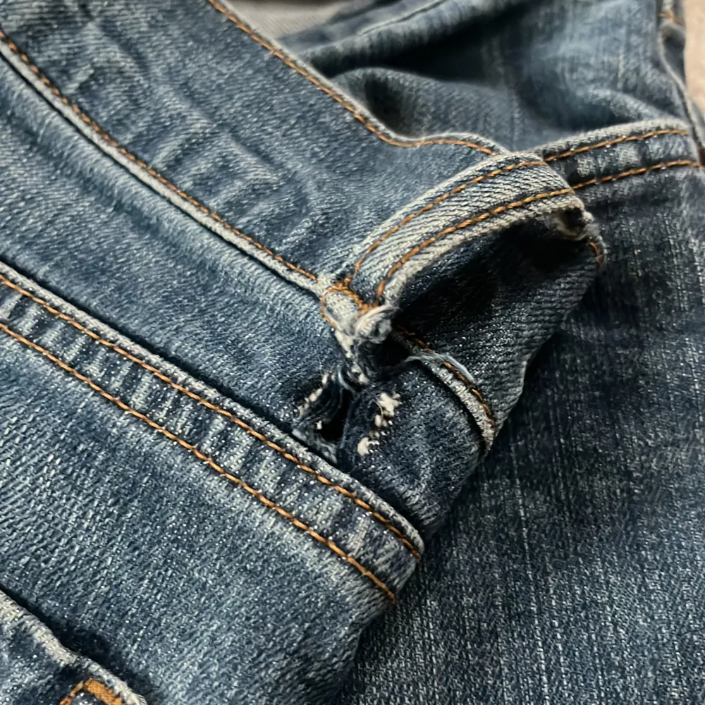 Säljer ett par klassiska blå jeans från Lindex. De har en blandning mellan rak och bootcut passform med femficksdesign och knappgylf. Perfekta för en avslappnad stil. Jeansen har tyvärr ett hål på båda sidorna som syns på sista bilden men går super enkelt att fixa med lite nål och tråd! Original priset ligger mellan 400-700kr.. Farkut & Housut.