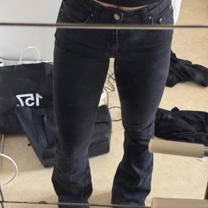 Svarta jeans - Snygga svarta jeansbyxor med en tight passform och låg midja. De har klassisk femficksdesign och knappar framtill. Perfekta för en stilren look. 