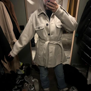 Beige kappa med bälte - Snygg beige kappa med bälte och knappar framtill. Jackan har långa ärmar och två stora fickor med lock på bröstet. Perfekt för höst och vår. Pris går att diskutera. 