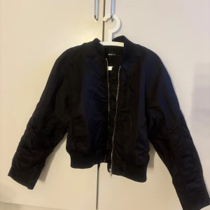 Svart bomberjacka från Gina Tricot - Snygg svart bomberjacka från Gina Tricot i storlek M. Jackan har en dragkedja framtill och är perfekt för en cool stil. Den har långa ärmar och en klassisk bomberjacka-look. Aldrig använd 
