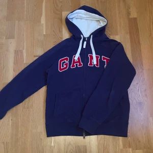 Blå full zip hoodie  - Säljer en riktigt skön och snygg GANT hoodie. Den är i storlek L men passar mer i M, enligt mig. Skriv vid några funderingar!