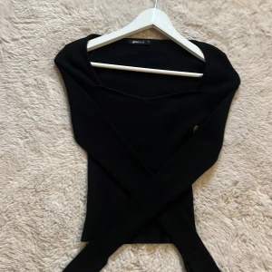 Svart topp Gina Tricot - Snygg svart långärmad topp med en omlott-design från Gina Tricot. Tillverkad i ett mjukt och bekvämt material. Toppen är aldrig använd och är i toppen skick! 