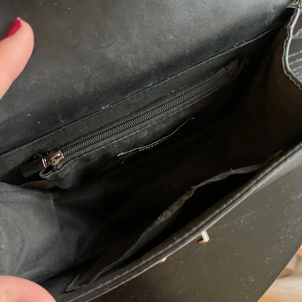 Snygg svart axelväska från Ginatricot med quiltat mönster och kedjedetaljer. Väskan har en praktisk dragkedja inuti och en elegant låsdetalj framtill. Kedjan går att justera och ha crossbody.. Laukut & Käsilaukut.