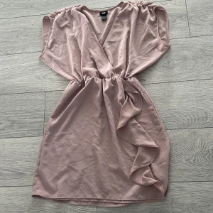 Ljusrosa omlottklänning från H&M - Säljer en söt ljusrosa omlottklänning från H&M. Klänningen har en v-ringad design och fina volangdetaljer på sidan. Perfekt för sommarens alla tillfällen! 💖