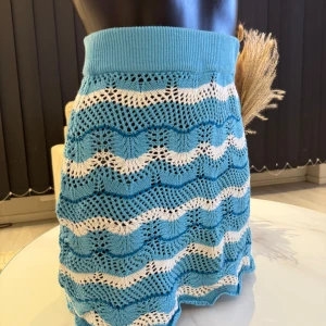 Blå och vit stickad kjol - Säljer en söt blå och vit stickad kjol med vågigt mönster. Kjolen har en elastisk midja och är perfekt för en avslappnad stil. Den är kort och har en luftig design som passar bra till varmare dagar. Passar perfekt i /L storlek.🌸🌸