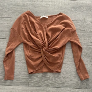 Brun ribbad topp från Outrageous Fortune - Säljer en snygg brun ribbad topp från Outrageous Fortune. Toppen har en unik knytdetalj framtill och långa ärmar. Perfekt för att ge din outfit det lilla extra!