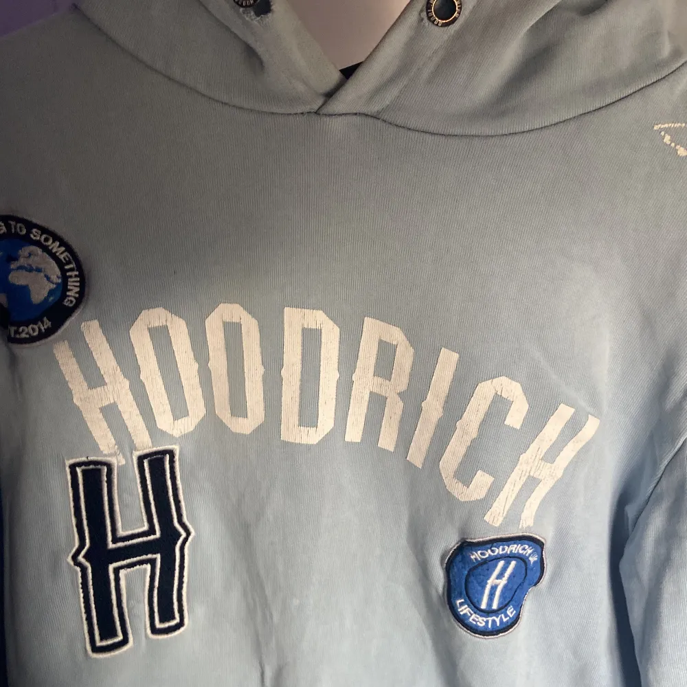 Säljer en ljusblå hoodie från Hoodrich med tryck och patchar på framsidan. Den har en klassisk känguruficka och en bekväm huva med dragsko. Perfekt för en avslappnad stil. Varan finns ej kvar på hemsida.. Neuletakit & Villapaidat.