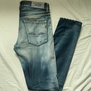 Replay jeans med sjuk fade/slitningar - Säljer ett par unika snygga Replay jeans Geebo (slim fit) i ljusblå tvätt med slitningar och och små röda detaljer. Jeansen har normal passform, raka/slim ben. Storlek 31/34 och passar mig perfekt som är 193cm 77kg. De har hål i knäna och ett litet i/under skrevet som ej syns.