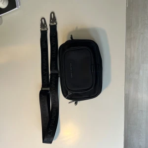 Svart axelväska från Daily Paper - Säljer en svart axelväska från Daily Paper med justerbar rem där loggan är invävd. Väskan har två stora fack med dragkedja och ett mindre ytterfack. Insidan är fodrad med mönstrat tyg.