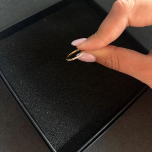 Guldfärgad ring med stenar från Edblad - Superfin tunn guldfärgad ring från Edblad, dekorerad med små gnistrande vita stenar runt hela ringen. Perfekt för dig som gillar stilrena och eleganta smycken med lite extra bling. Passar snyggt att bära ensam eller att stapla med andra ringar.