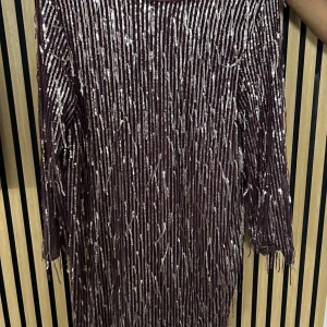 Vinröd glittrig kortklänning med paljetter - Vinröd kortklänning från Zara med glittriga silverpaljetter i vertikala ränder. Klänningen har v-ringning, trekvartsärm och fransiga detaljer längst ner. Perfekt för dig som vill sticka ut med en festlig look. Aldrig använd och fortfarande med prislapp. Ordinarie pris är 715 