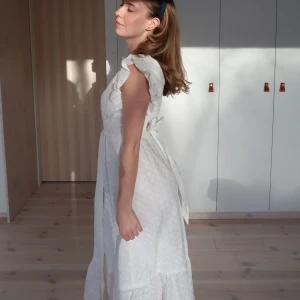 Vit somrig långklänning med volang - Superfin vit långklänning med broderade små blommor, volangärmar och knytband i midjan. Klänningen har en luftig passform och är perfekt för varma dagar. Söt och romantisk stil med omlottkänsla och v-ringning. Nypris 1600kr