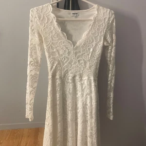Vit spetsklänning från Bubbleroom - Superfin vit klänning från Bubbleroom med lång ärm och v-ringad hals. Klänningen har ett vackert blommigt spetsmönster och är helfodrad. Perfekt för dig som vill ha en romantisk och elegant look. Sitter snyggt i midjan och har en lätt utställd kjol.