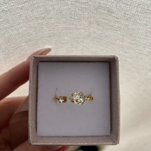Guldring  - Trendig guldfärgad ring med tvinnad design och två gnistrande stenar.  Ringen har öppen front och ger en lyxig känsla med sina klara stenar som fångar ljuset snyggt.
