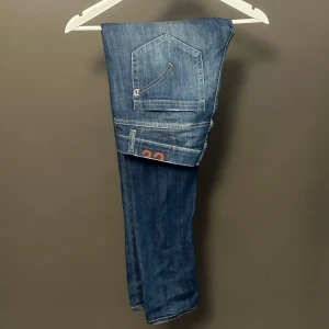 Blå Domdip jeans med orange detalj - Snygga blå jeans från Dondup med coola orangea detaljer och kontrastsömmar. Klassisk femficksmodell med smal passform och lätt slitning på låren. Bakfickorna har unik sömnad och jeansen har en modern look som passar till det mesta.