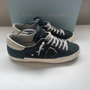 Philippe Model mörkgröna/navy sneakers i skinn - Snygga mörkgröna/navy sneakers från Philippe Model med vita detaljer och snörning. Skorna har en klassisk låg siluett, vit sula och är tillverkade i skinn med mockadetaljer. Perfekta för dig som gillar stilrena och trendiga sneakers.