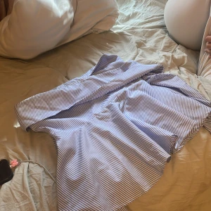 Blåvit randig skjorta med krage - Snygg skjorta med smala blå och vita ränder och klassisk krage. Skjortan har lång ärm och knäppning framtill. Perfekt för dig som gillar en stilren och fräsch look.