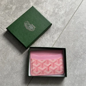 Rosa Goyaard plånbok - Supersnygg rosa plånbok från Goyaard med deras ikoniska grafiska mönster. Plånboken har flera kortfack och är tillverkad i skinn med en lyxig känsla. Perfekt för dig som vill ha något unikt och stilrent i väskan.
